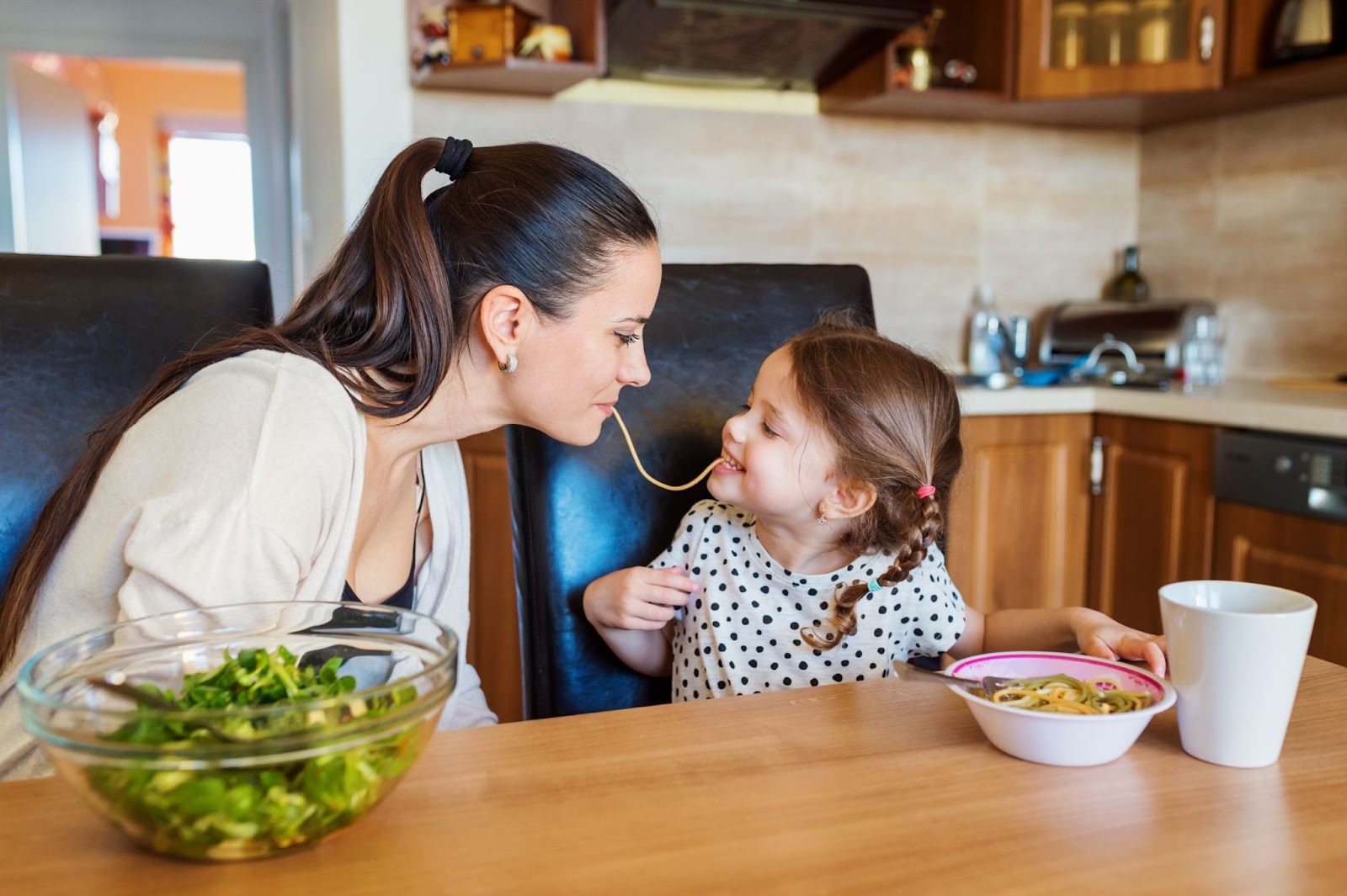 Üç çocuklu anne ve kızı birlikte makarna ve sebze salatası yiyor çocuklarda yeme davranışı