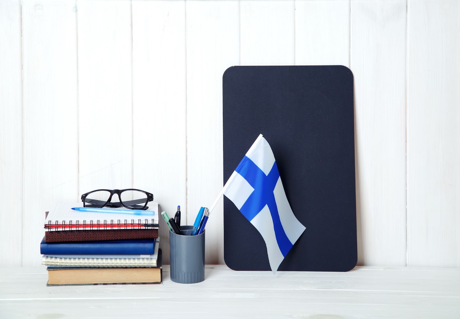 Kitaplar, defterler, ders kitapları, gözlükler, ahşap bir masa üzerinde Finlandiya bayrağı. Finlandiya'da eğitim.